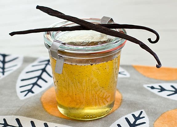 A glass wreck jar with vanilla syrup inside. There are two vanilla beans resting on top of the jar.