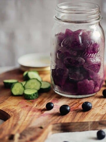 A jar of purple smoothie ice cubes with cucumbers and blueberries.
