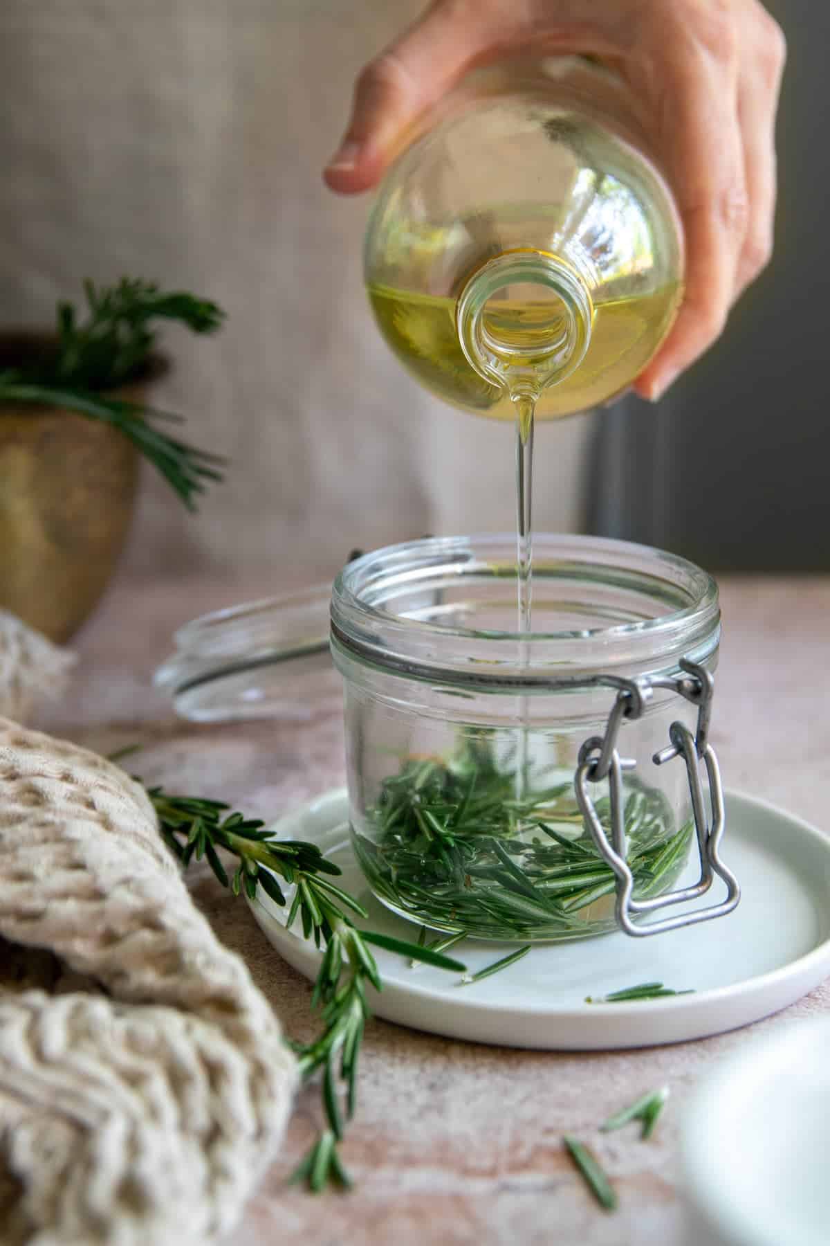 Pouring carrier oil over fresh rosemary for infusion